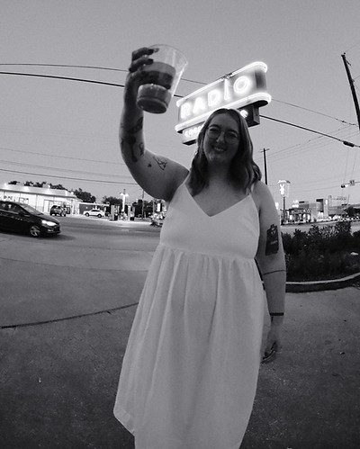 Julia cheers with coffee in front of coffee sign
