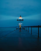 vertical-distant-shot-person-holding-umbrella-walking-footbridge-near-lighthouse.jpg