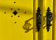 Black wrought-iron door handles casting shadows on a bright yellow door at Bar Sevillano in Nerja