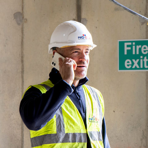 Construction working wearing hard hat on mobile phone.