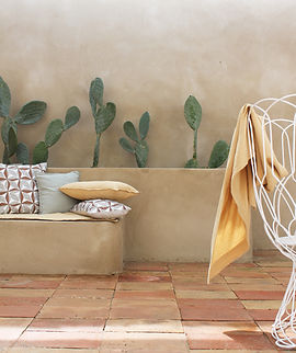 Photo d'ambiance des articles de décoration de la marque Blanc Cerise (plaid, coussins) sur une terrasse extérieure sous une pergola