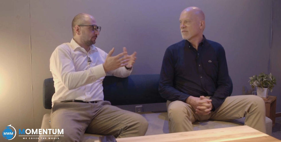 Jeremy Laughlin and David Price sitting on a couch in a studio, one gesturing while talking.