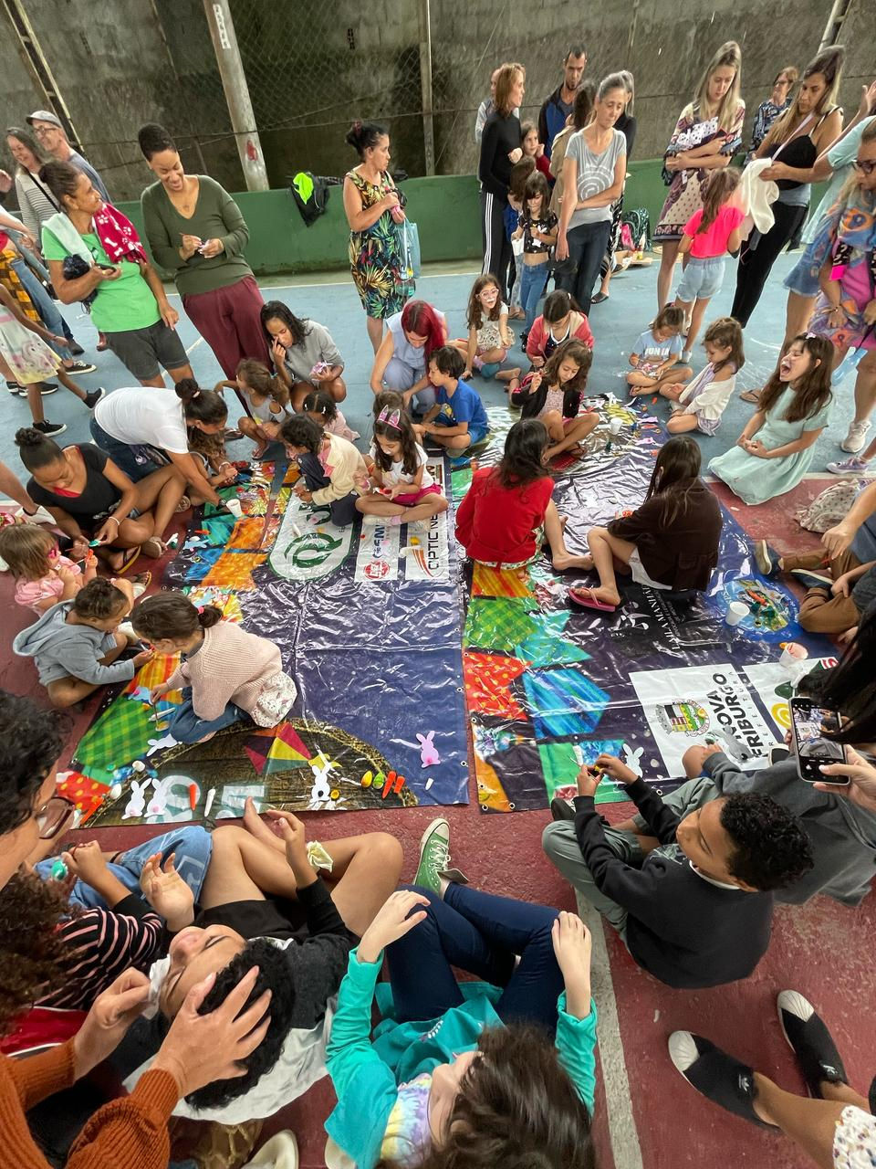 Crianças e adultos participam de atividade com painéis coloridos.