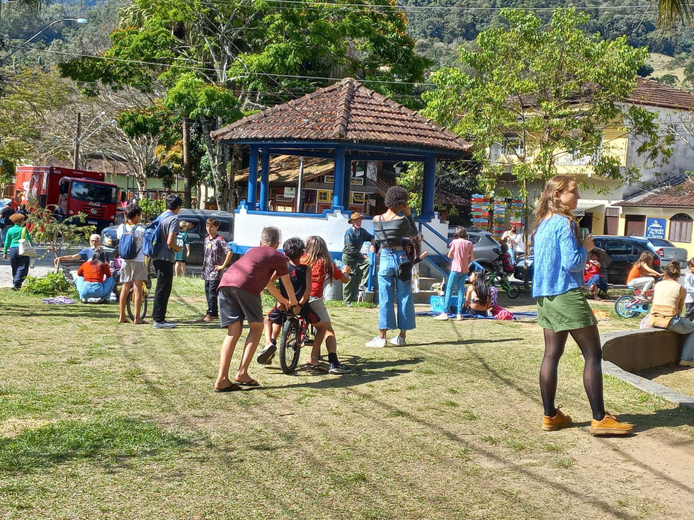 Crianças brincando com adultos em gramado ao lado de coreto.