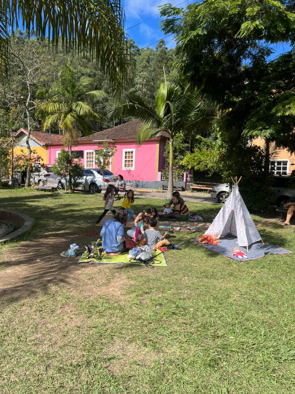 Crianças e adultos em piquenique no gramado com uma tenda.