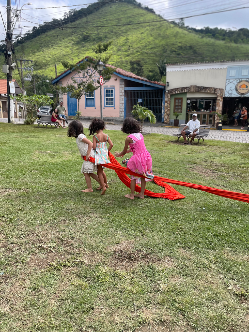 Três meninas brincando com fita vermelha na grama