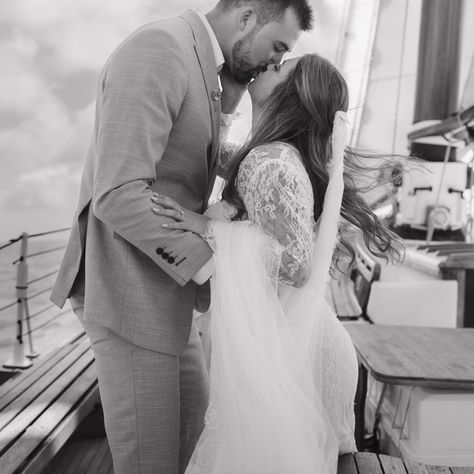 A bride and groom kiss in a black and white photo on a sailboat.