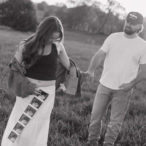 A woman holds her pregnant belly and a sonogram, while her other hand holds her husband's (who is walking behind her).