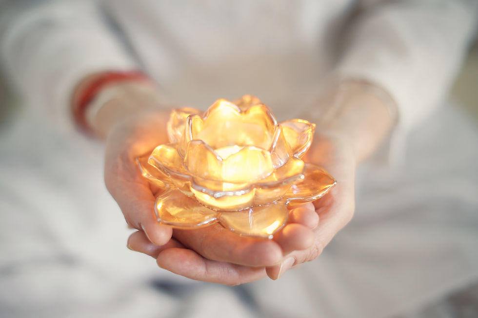 Small burning candle in an transparent orange lotus shaped glass candle holder laying on s