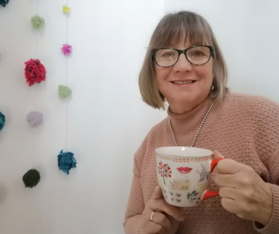 Caroline, smiling with a cuppa in hand.