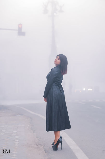 Fashion editorial portrait of a woman in a black leather dress on a misty street