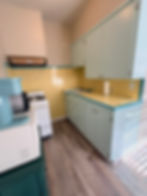 Studio apartment kitchen showing stove, sink, cabinets, coffee maker and microwave