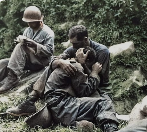 PFC George Paul Gutzman consoling another soldier whose friend had just been killed in action, while another soldier in the background fills out a casualty tag. The soldier being consoled was also killed in action mere hours after this photo was taken in Haktong-ni area, Korea. Public domain photo by American military photographer Al Chang (Army); Colorized by Jared Enos.