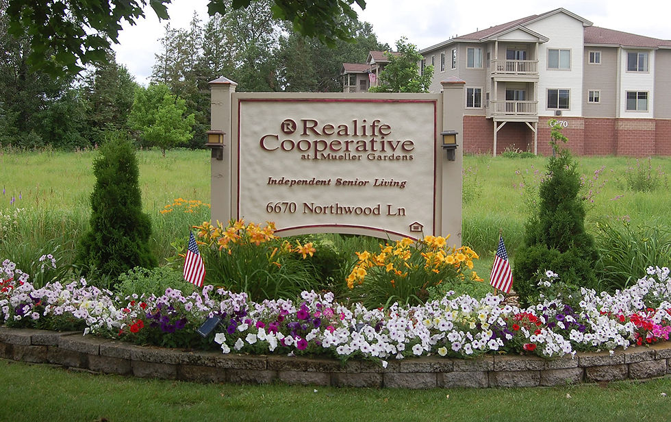 The Realife Cooperative at Mueller Gardens sign is nestled among flowers planted by residents. Photo by Scott Thoma