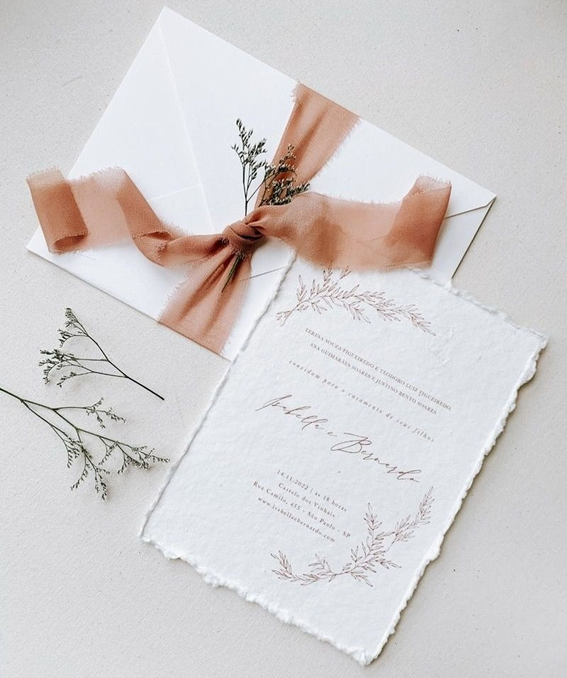 White eco-friendly wedding invitation crafted from recyclable paper, elegantly tied with a pink ribbon.