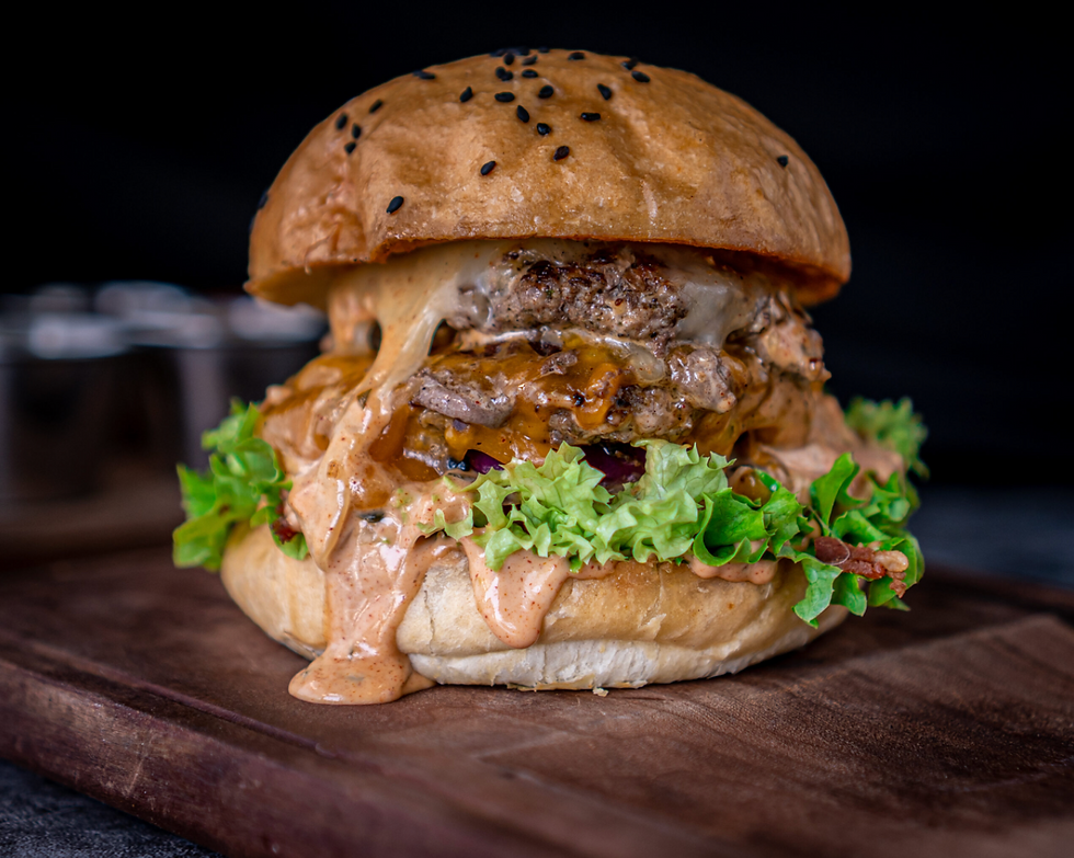 Juicy cheeseburger with lettuce, dripping sauce, and sesame seed bun on wooden board. Rich texture, dark background. Mouthwatering and appetizing.