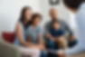 Happy young family sitting on couch and talking with family counselor. Smiling parents wit