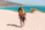 Happy guy carrying a girl on his back walking in the sand along the beach