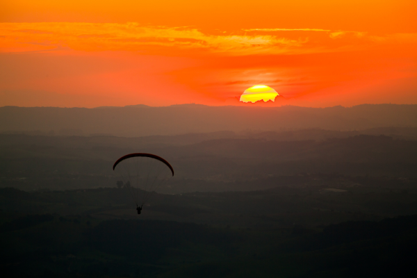 Pessoa meditando ao pôr do sol na Pedra Grande em Atibaia, cercada por montanhas e natureza exuberante