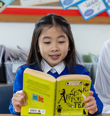 A child reading a book at school to her teacher