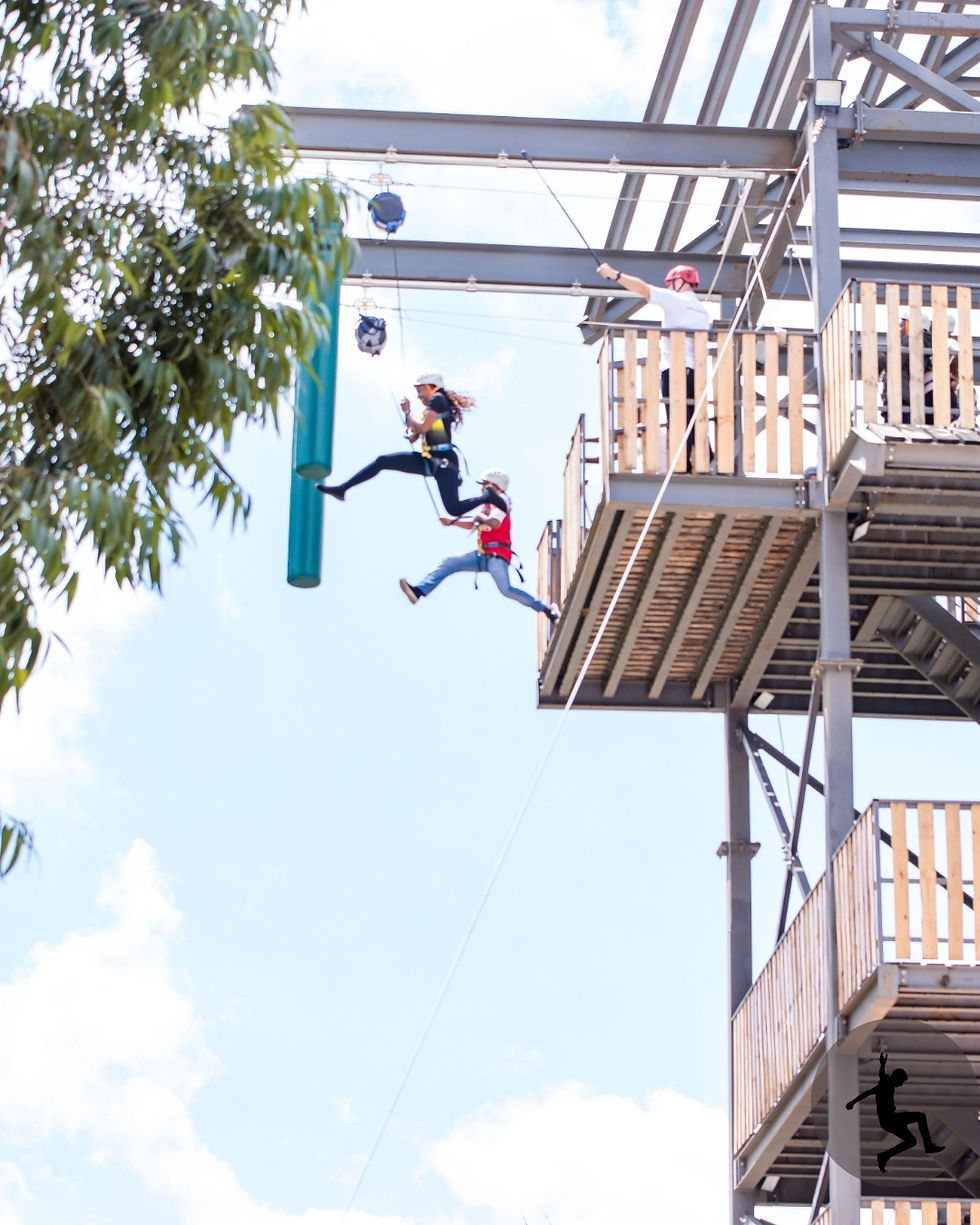 A man and woman take an exhilarating 13-meter plunge during the Leap of Faith activity, showcasing their adventurous spirit against a bright sky.