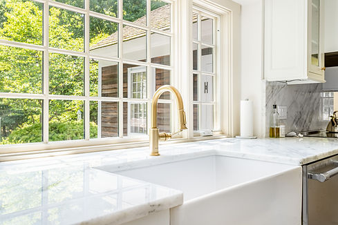 Modern kitchen with brass faucet, marble counters, and garden view