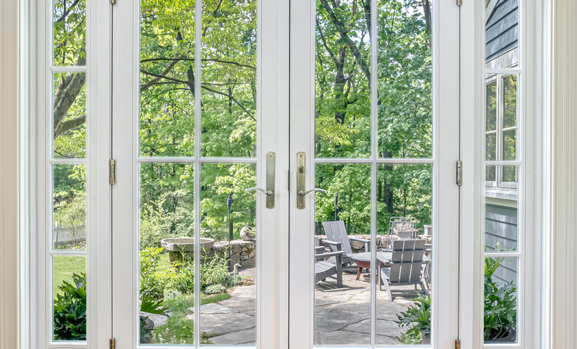 White French doors opening to a patio and lush green woods