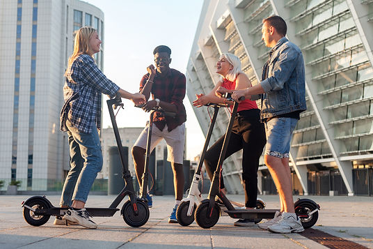 interracial group of young friends ride electric scooters in the city and communicate, mul