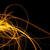 A macro photo of golden light trails weaving across a black background, captured with long