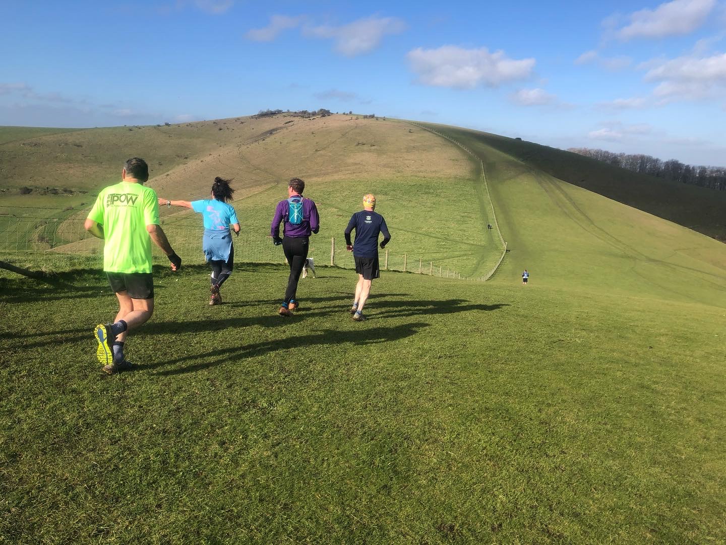 Group running across steep, undulating grassy terrain.
