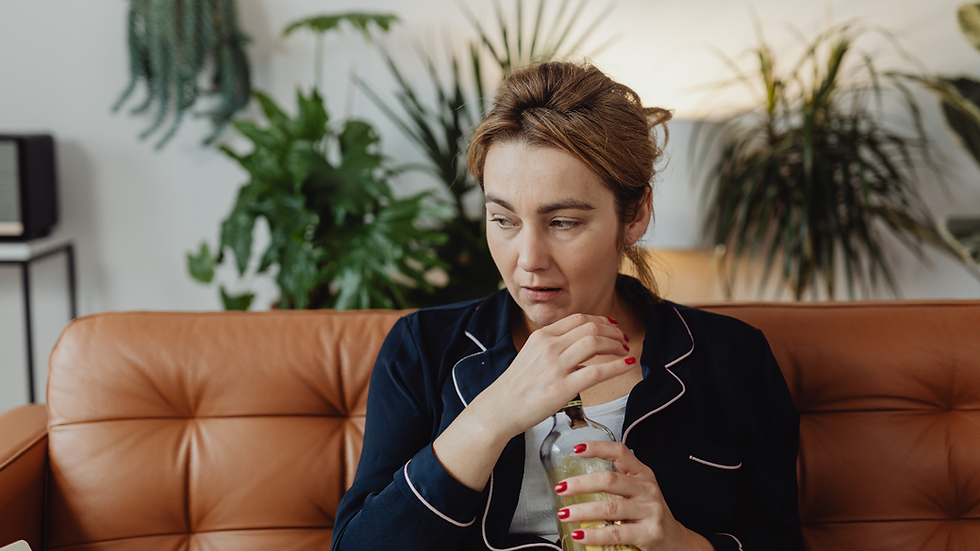 Woman holding a drink bottle on a couch, looking worried as she considers not drinking.