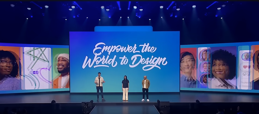 Three people stand on stage with a large screen displaying "Empower the World to Design." Colorful graphics and smiling faces surround them.