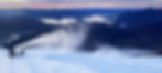 En snökanon sprutar snö i en skidbacke vid solnedgång, med utsikt över en dalgång och en stor sjö omgiven av berg. Himlen är färgad i rosa och orange toner, och en person rör sig intill snökanonen i bakgrunden.
