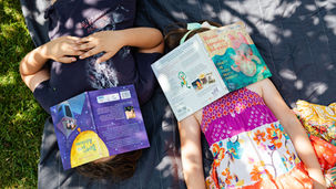 Bambini distesi su un prato che hanno il volto coperto da libri