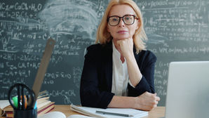 Un'insegnante donna posa con sicurezza davanti alla lavagna con delle equazioni.