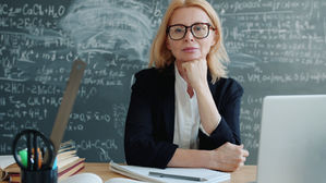 Un'insegnante donna posa con sicurezza davanti alla lavagna con delle equazioni.