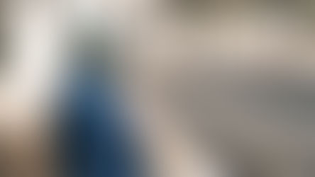 Una donna con un cappotto blu e hijab aspetta in una stazione di treni all'aperto vuota.