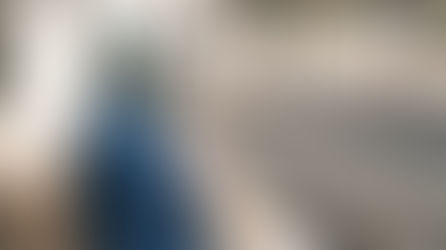 Una donna con un cappotto blu e hijab aspetta in una stazione di treni all'aperto vuota.