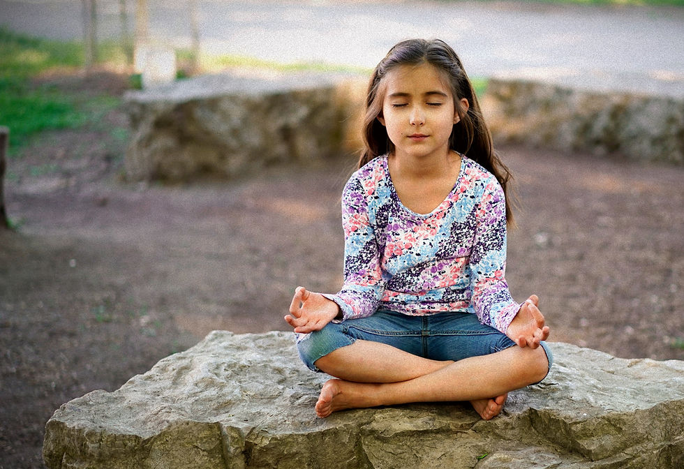 young girl meditating outdoors on a large rock