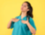 Woman in teal scrubs stands against a yellow background, hands on chest, with a relaxing pose