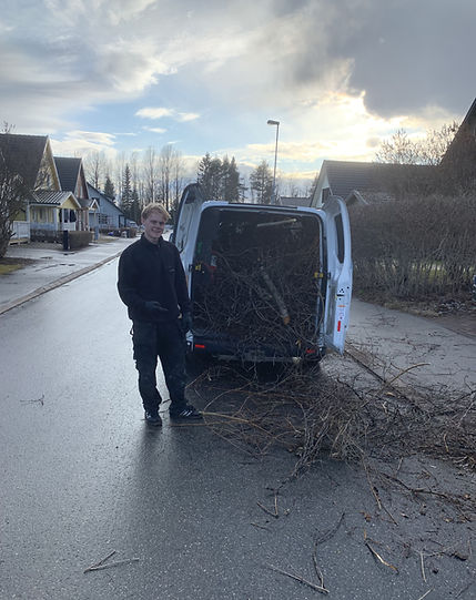 En person står vid en arbetsbil med trädgårdsavfalls om ska bortforslas.
