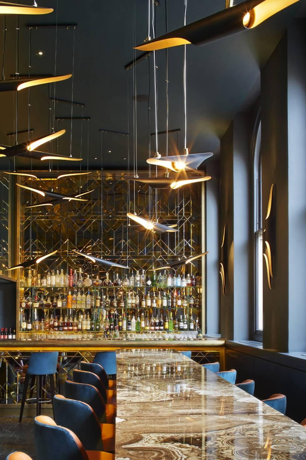 Premium cocktail bar interior featuring statement pendant lighting, marble communal table, premium bar display, and dramatic contemporary hospitality design.