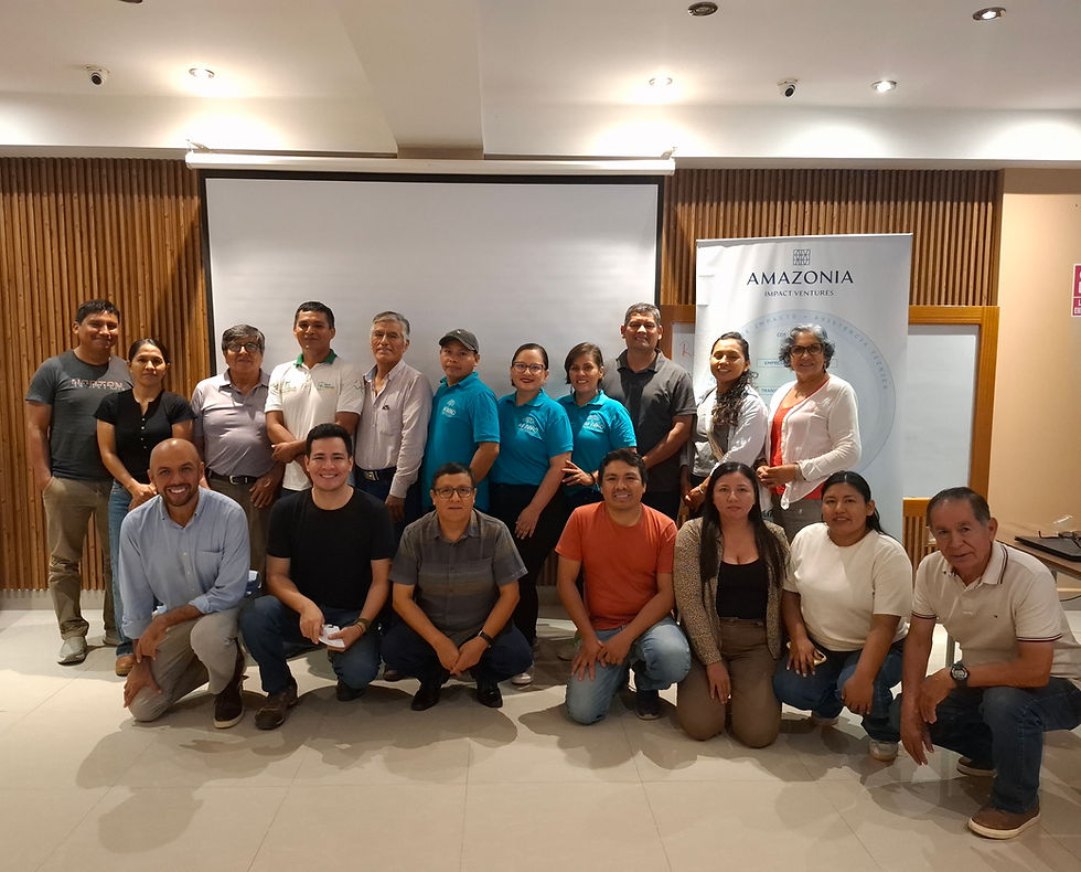 A group of seventeen participants pose for a photo in a conference room during an Amazonia Impact Ventures workshop, standing and kneeling in front of a projection screen and an AIV banner.