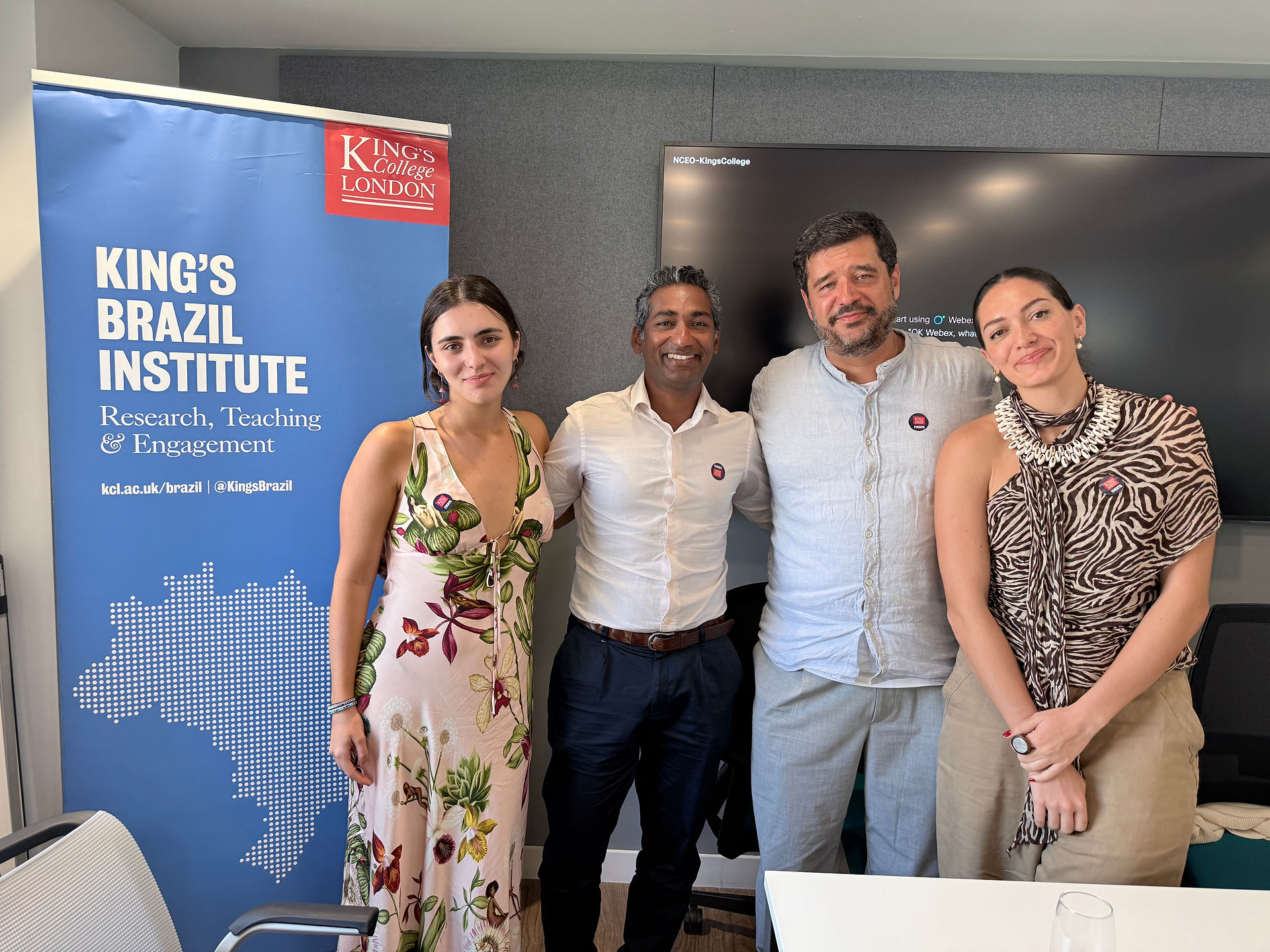 Four participants standing together in front of a King’s Brazil Institute banner, smiling for a group photo.