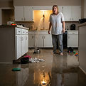 A white mom in her house looking at a flooded kitchen from a burst water pipe.jpg