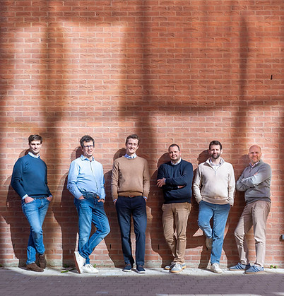 Six hommes debout, l'air détendu, adossés à un mur de briques