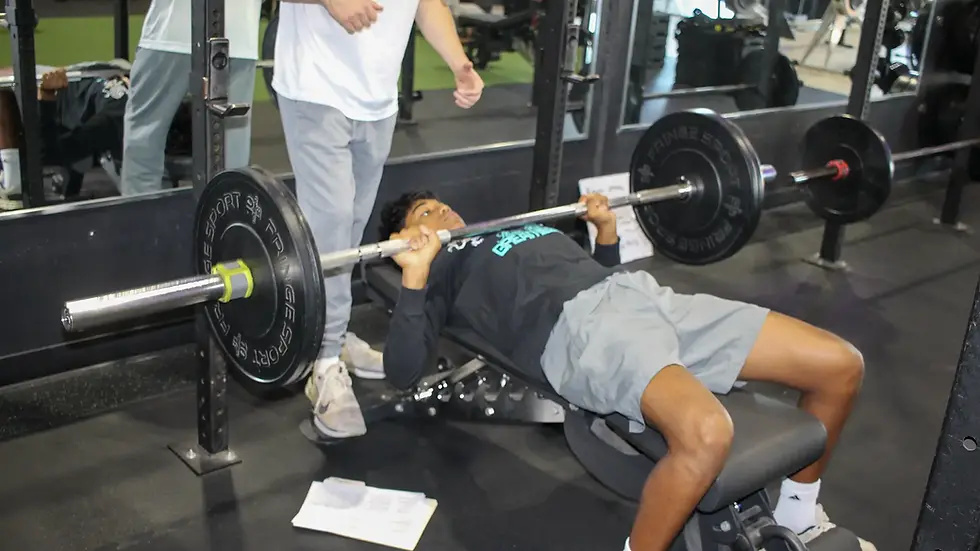 Coach supervising a youth athlete during progressive warm-up sets before strength training