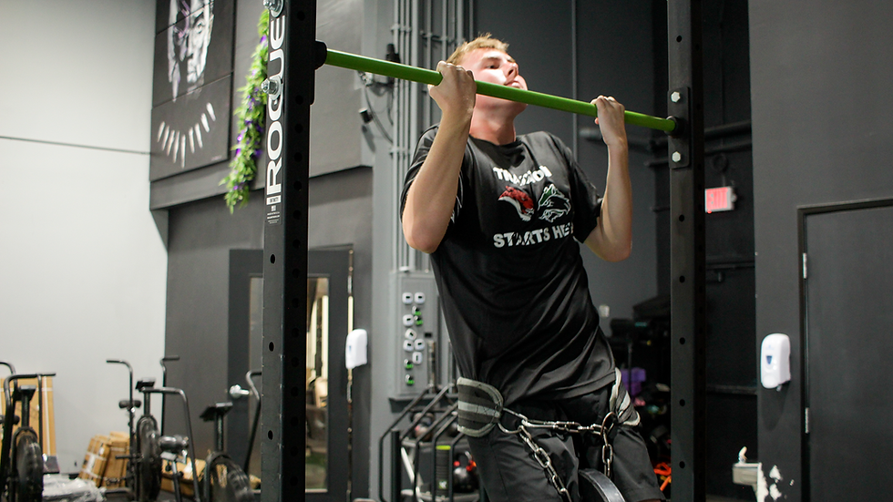 High school athlete performing a weighted pull-up during a supervised strength session