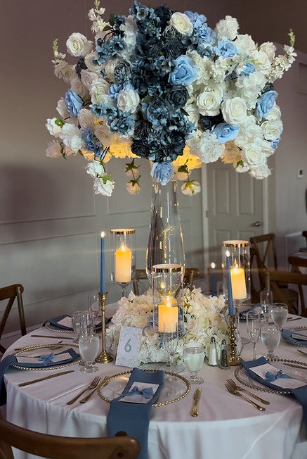 Soft blue and white floral centerpiece with gold candle holders and romantic wedding table décor.
