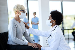 black-doctor-mature-patient-wearing-protective-face-masks-while-talking-waiting-room-clini